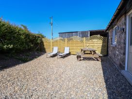 An outdoor gravel patio with two lounge chairs, a wooden picnic table, and a wooden fence at Bwthyn Taid in Holywell