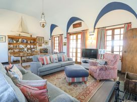 A living room with blue sofas a patterned armchair a wooden shelving unit and arched windows at Borth Arian in Rhoscolyn