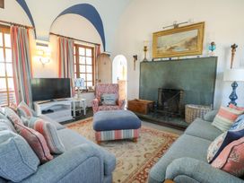 A living room with two sofas a large ottoman a fireplace a television and windows with curtains at Borth Arian in Rhoscolyn