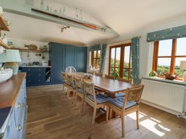 A dining area with a wooden table and chairs next to windows and blue cupboards in a kitchen at Borth Arian in Rhoscolyn