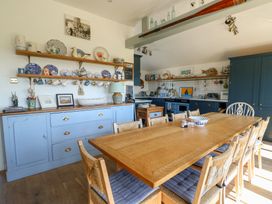 A kitchen with a wooden dining table and wicker chairs with blue cushions at Borth Arian in Rhoscolyn