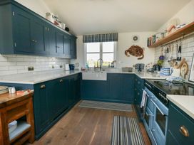 A kitchen with blue cabinets white countertops a wooden table under a window and striped rugs at Borth Arian in Rhoscolyn