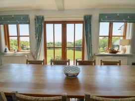 A dining room with a wooden table and chairs looking out to a garden through glass doors at Borth Arian in Rhoscolyn
