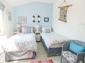 A bedroom with two single beds a blue accent wall a wicker chair and nautical decor at Borth Arian in Rhoscolyn