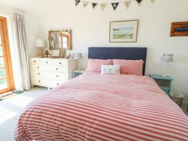 A bedroom with a bed with red and white striped bedding a white dresser with a mirror and a blue bedside table at Borth Arian in Rhoscolyn