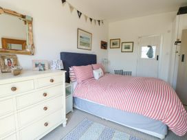 A bedroom with a bed with red and white striped bedding a cream dresser with photos and a mirror and framed pictures on the wall at Borth Arian in Rhoscolyn