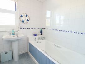 A bathroom with a pedestal sink and bathtub with blue and white tiles and a decorative lifebuoy on the wall at Borth Arian in Rhoscolyn
