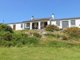 A white house with columns and a porch on a grassy hill under a clear blue sky at Borth Arian in Rhoscolyn