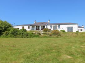 A white single-story house with multiple doors and windows surrounded by grass and shrubs at Borth Arian in Rhoscolyn
