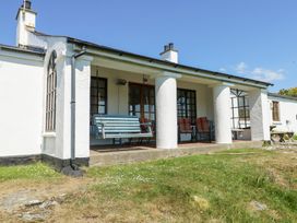 A porch with a blue swing and two chairs with cushions outside a white house at Borth Arian in Rhoscolyn