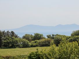 A view of trees and green grass with water and mountains in the background at Borth Arian in Rhoscolyn