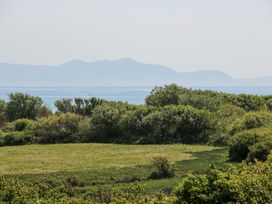 A grassy field with bushes and trees and a body of water and distant hills in the background at Borth Arian in Rhoscolyn