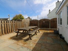 An outdoor patio with a wooden table and fence at Farm Cottage in Cemaes Bay