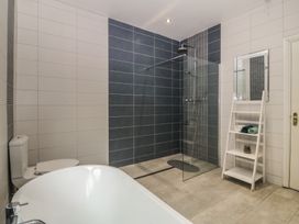 A bathroom with a bathtub, shower, and shelving unit at Gwylan Uchaf Y Felinheli