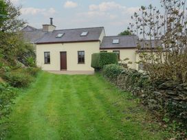 A cottage with a door and windows surrounded by grass and a stone wall at Tyn y Mynydd Bull Bay
