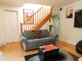 A living room with a gray sofa a black and orange coffee table and wooden stairs at Y Stabl in Criccieth