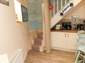 A small kitchen area with coffee appliances and mugs under a staircase with rope wrapped around a post at Y Stabl in Criccieth