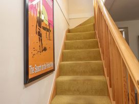 A staircase with yellow carpet and wooden railing next to a surf poster on the wall at Y Stabl in Criccieth