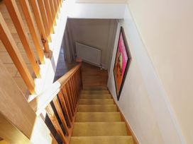 A staircase with yellow carpet and wooden handrails leading down to a hallway with a radiator and a framed poster on the wall at Y Stabl in Criccieth