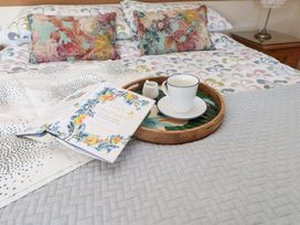 A bed with floral pillows and patterned bedding with a book and a tray holding a cup and a small pitcher on it at Y Stabl in Criccieth