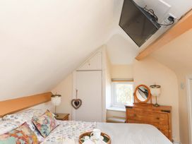 A bedroom with a bed a wooden dresser a wall-mounted TV and a small window at Y Stabl in Criccieth