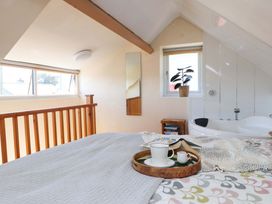 A bedroom with a bed a wooden railing a window and a bathtub at Y Stabl in Criccieth