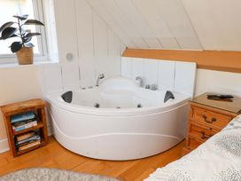 A corner bathtub next to a window with a plant on the windowsill and wooden bedside tables with books and a remote control at Y Stabl in Criccieth