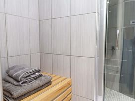 A corner of a bathroom with gray towels on a wooden bench and a glass shower door