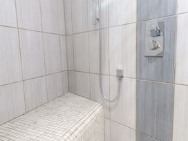 A tiled shower area with a built-in bench and a shower control at Y Stabl in Criccieth