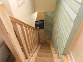 A staircase with wooden railing carpeted steps and blue wooden paneling on the wall at Y Stabl in Criccieth
