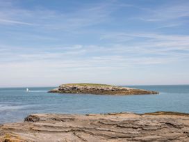 An island visible from a rocky shore with a boat in the sea at Llanallgo Church Rooms