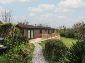 A wooden cabin with a deck and gravel path at Castell Chalet in Penrhos near Pwllheli