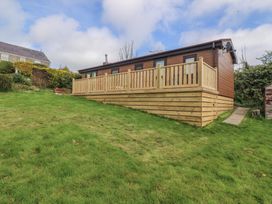 A wooden chalet with a deck in the garden at Castell Chalet Penrhos near Pwllheli