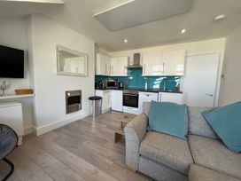 A small kitchen and living area with white cabinets blue backsplash grey sofa and a wall-mounted tv at Trevose in St Ives