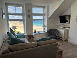 A living room with a sofa, pillows, armchair, TV, lamps, and windows overlooking a beach at Trevose in St Ives