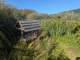 A garden with a wooden well surrounded by grass and plants at Minydon in Fairbourne