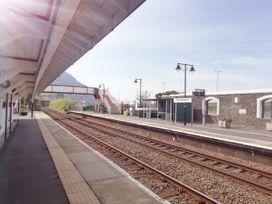 An empty train station platform with tracks and a pedestrian bridge at Penmaenmawr