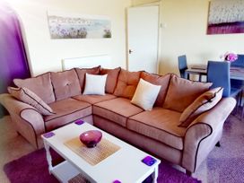 A living room with a brown sectional sofa white coffee table and a dining table with chairs at Llys Madoc The Top Flat in Penmaenmawr