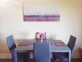 A dining table with four chairs flowers in a vase and placemats under a painting at Llys Madoc The Top Flat in Penmaenmawr