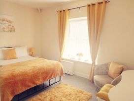 A bedroom with a bed yellow blanket and pillow a bedside table lamp a window with yellow curtains a chair with a yellow cushion and a rug at Llys Madoc The Top Flat in Penmaenmawr