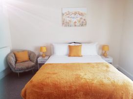 A bedroom with a bed with white and orange bedding two bedside tables with lamps a chair with an orange cushion and a painting above the bed at Llys Madoc The Top Flat in Penmaenmawr