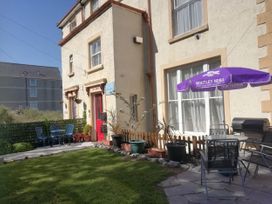 An outdoor patio area with chairs tables potted plants and an umbrella outside a building with a red door at Llys Madoc The Top Flat in Penmaenmawr