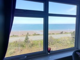 A window view showing a road, trees, a beach, and the sea at Llys Madoc The Top Flat in Penmaenmawr