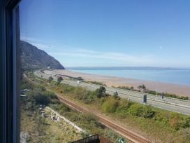 A coastal view with a mountain, roads, railway tracks, and a beach at Llys Madoc The Top Flat in Penmaenmawr