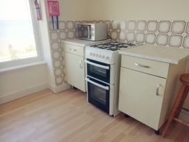 A kitchen corner with a gas stove, microwave on a counter, fire safety equipment on the wall, and cabinets at Llys Madoc The Top Flat in Penmaenmawr