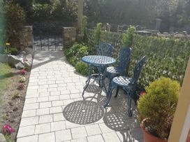 An outdoor patio with a blue metal table and three chairs surrounded by plants and a fenced garden at Llys Madoc The Top Flat in Penmaenmawr