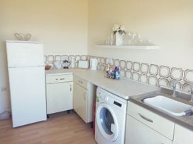 A kitchen with a refrigerator washing machine sink countertop and shelves with glassware at Llys Madoc The Top Flat in Penmaenmawr
