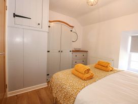A bedroom with a bed covered with yellow towels and patterned blanket near white wardrobes and a window at Yr Hen Dy Capel in Blaenau Ffestiniog
