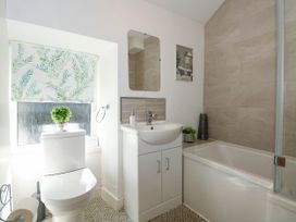 A bathroom with a toilet, sink, mirror, bathtub, plants, and a patterned window blind at Yr Hen Dy Capel in Blaenau Ffestiniog