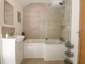 A bathroom with a white sink cabinet a bathtub with shower and glass screen and wall tiles in Yr Hen Dy Capel in Blaenau Ffestiniog